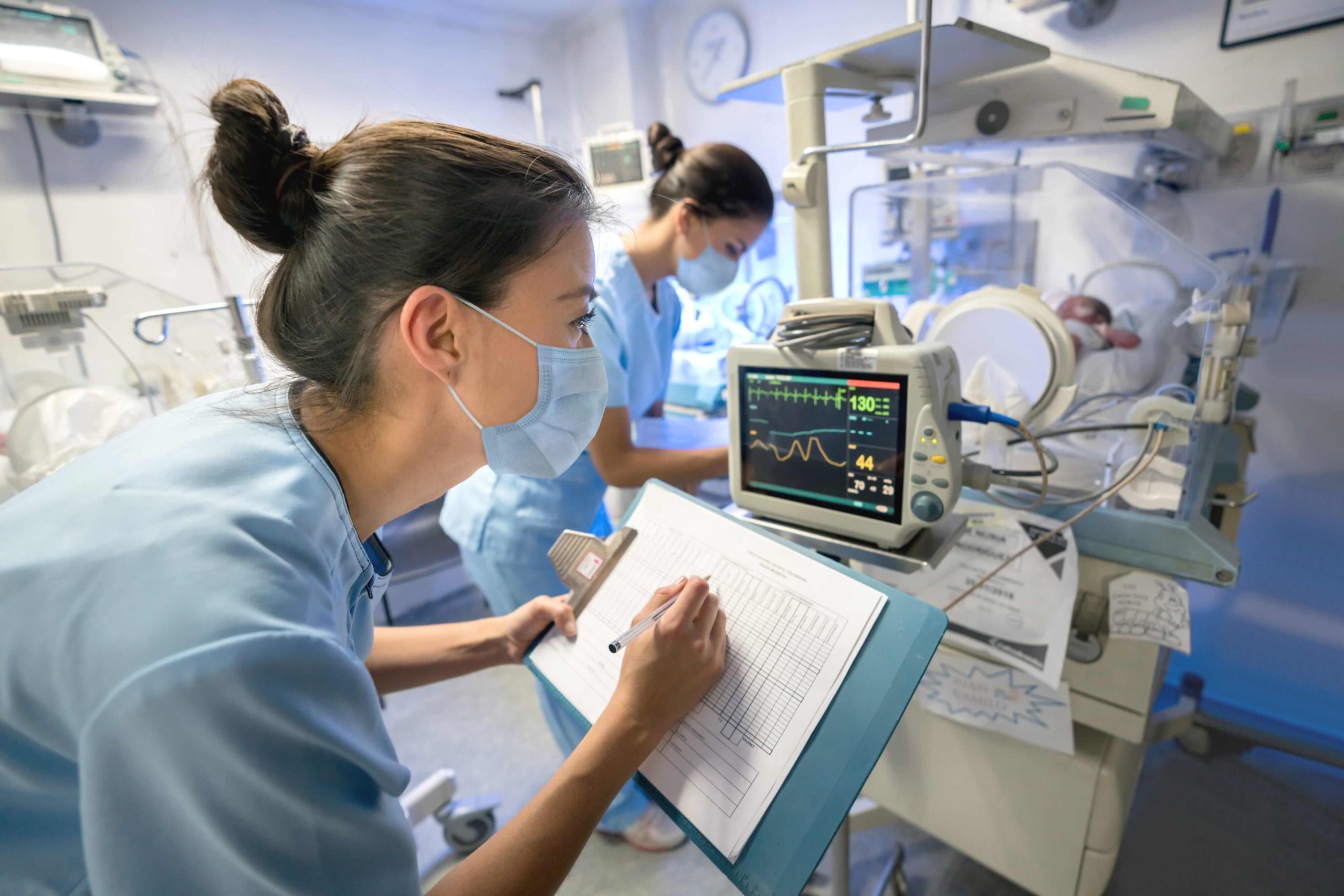 Clinician tracking neonatal vitals and recording performance metrics—illustrating data-driven ECMO program optimization.