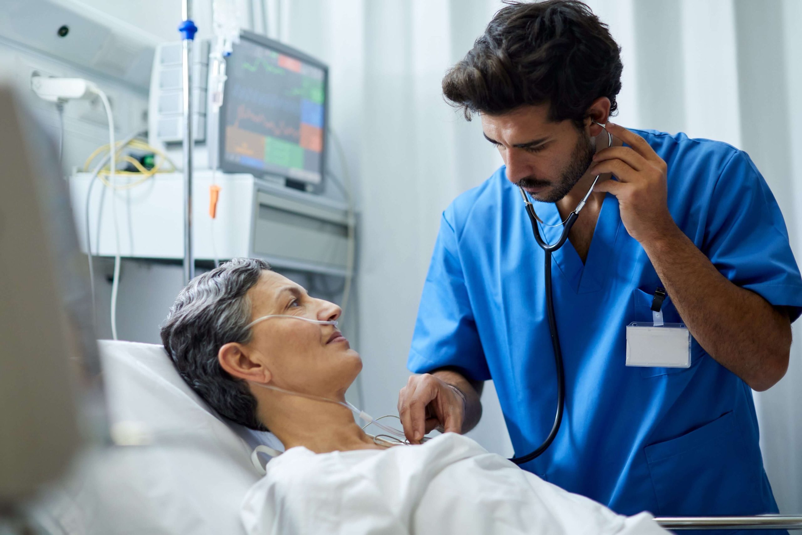 Clinician checking vital signs at a patient’s bedside using a stethoscope—providing attentive care and real-time cardiac monitoring.