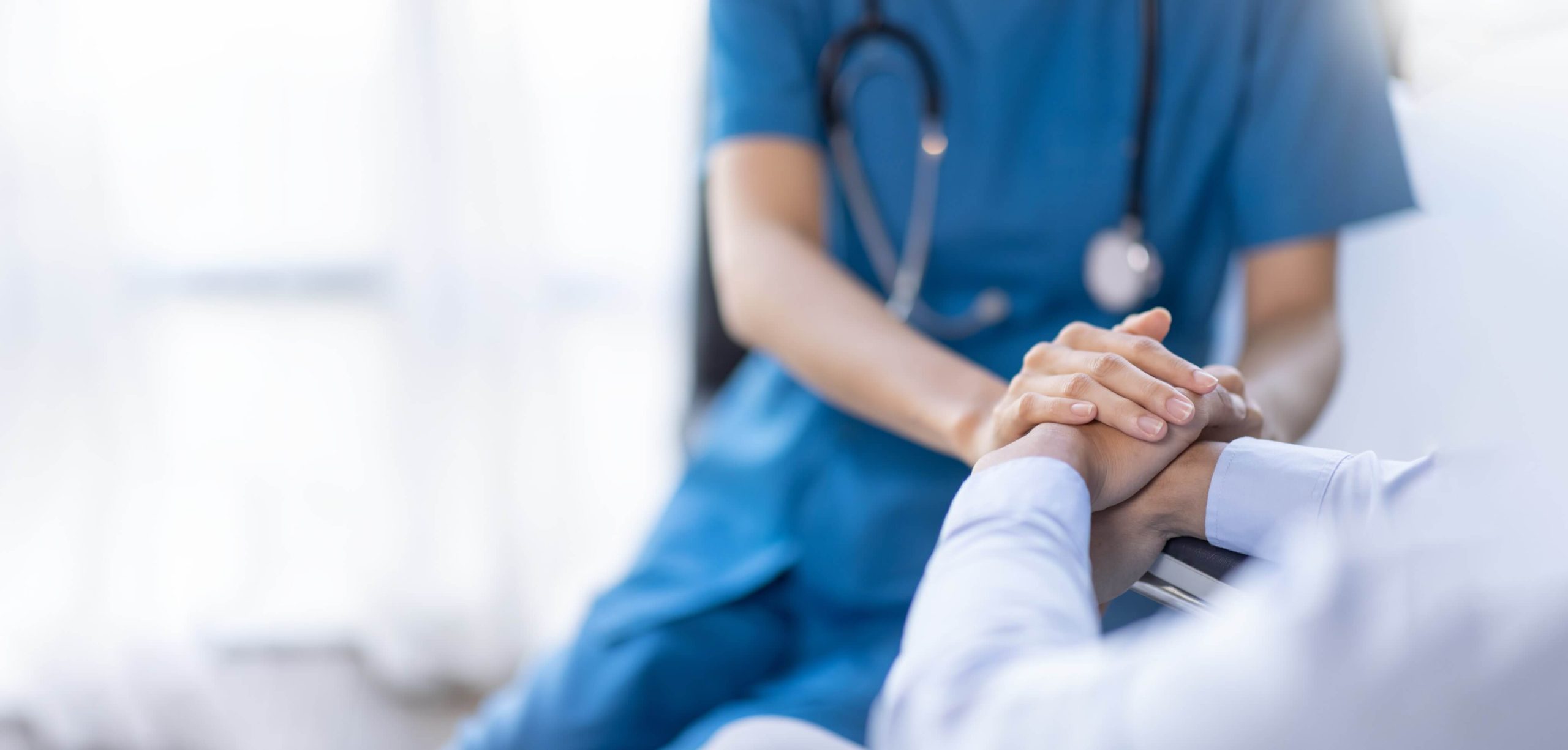 A clinician offering comfort and reassurance by holding a patient’s hand—human-first healthcare in action.