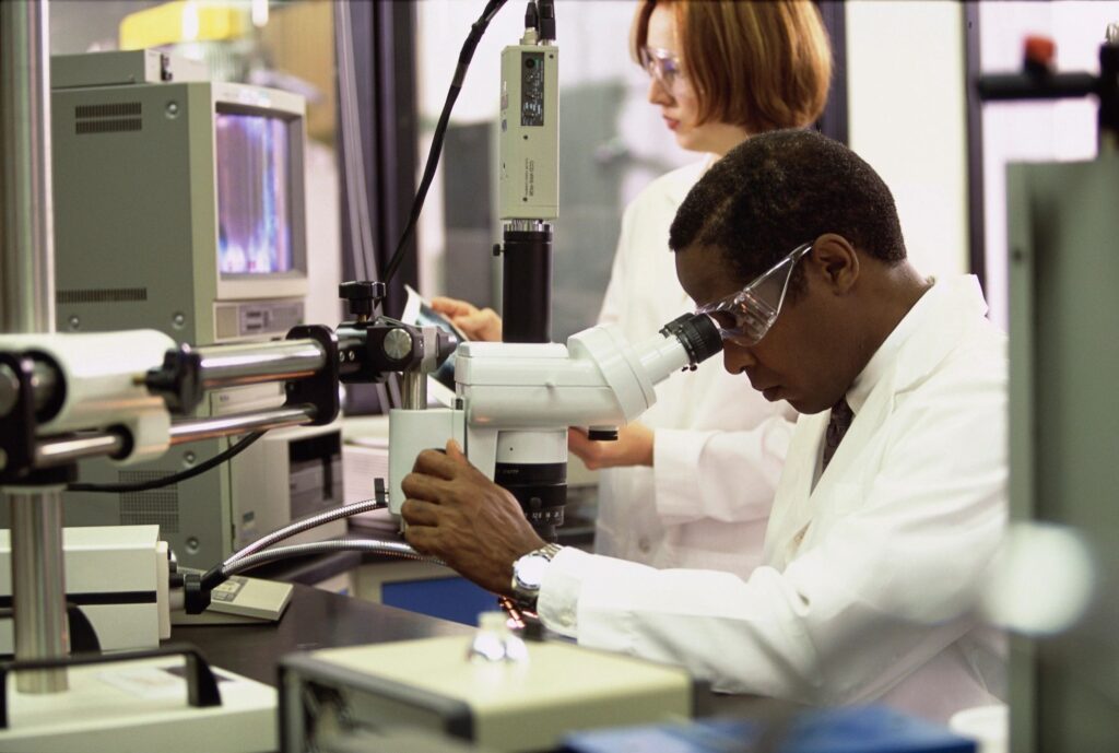 Medical researcher analyzing a sample under a microscope in a clinical lab—driving innovation and precision in care delivery.