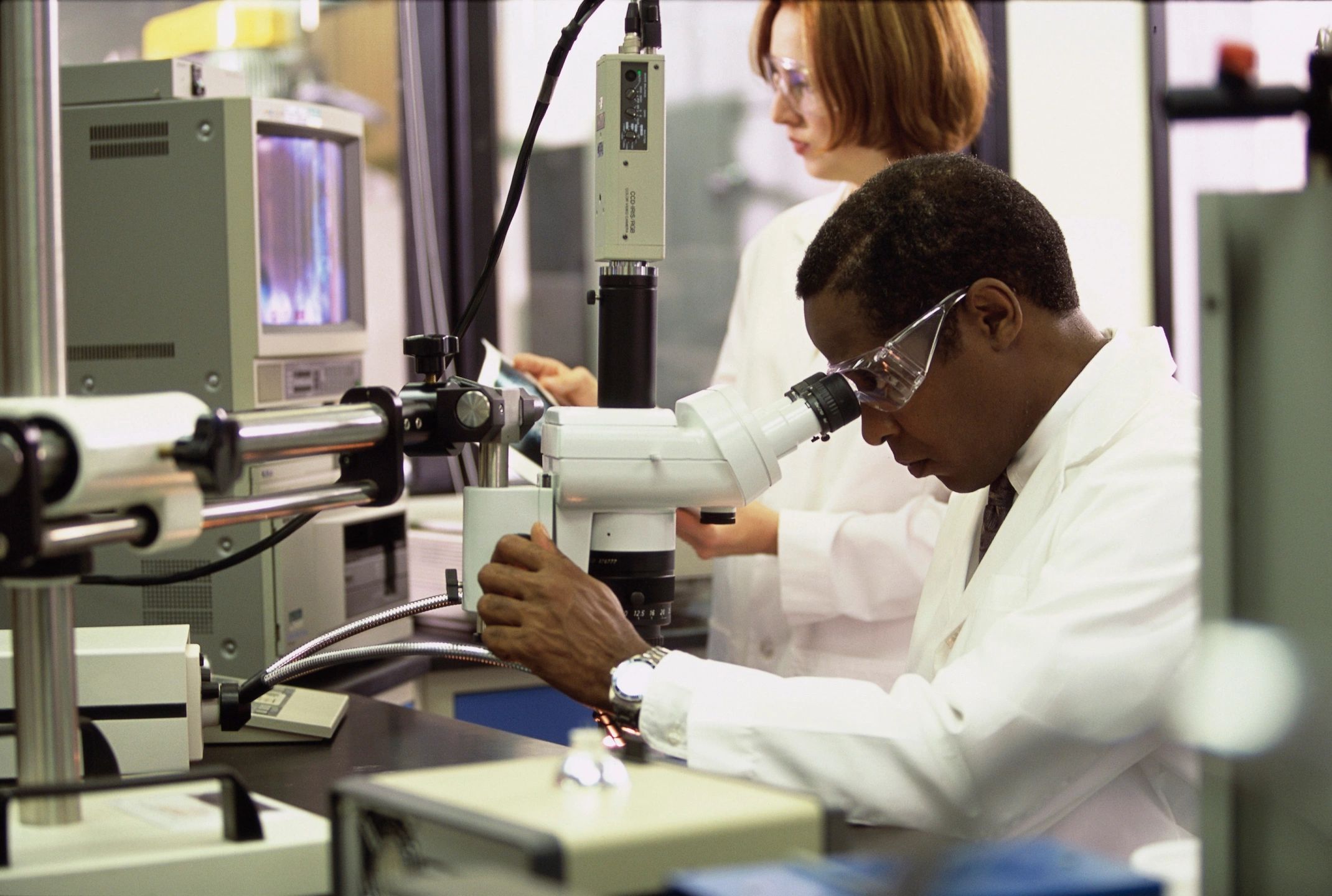 Medical researcher analyzing a sample under a microscope in a clinical lab—driving innovation and precision in care delivery.